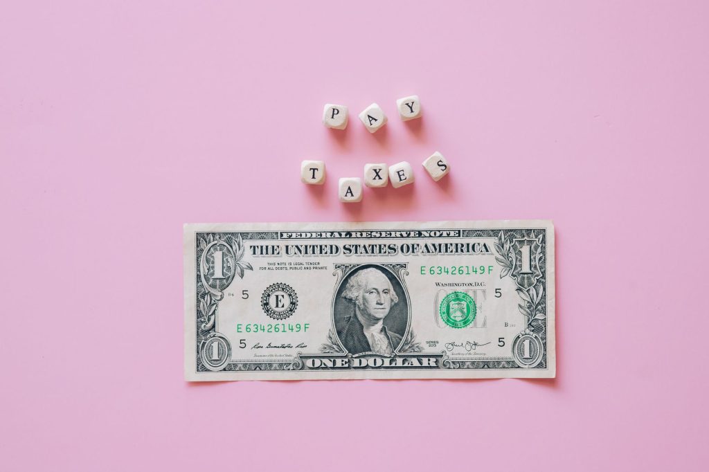 US one dollar bill on a pink background with pay taxes reminder cubes.