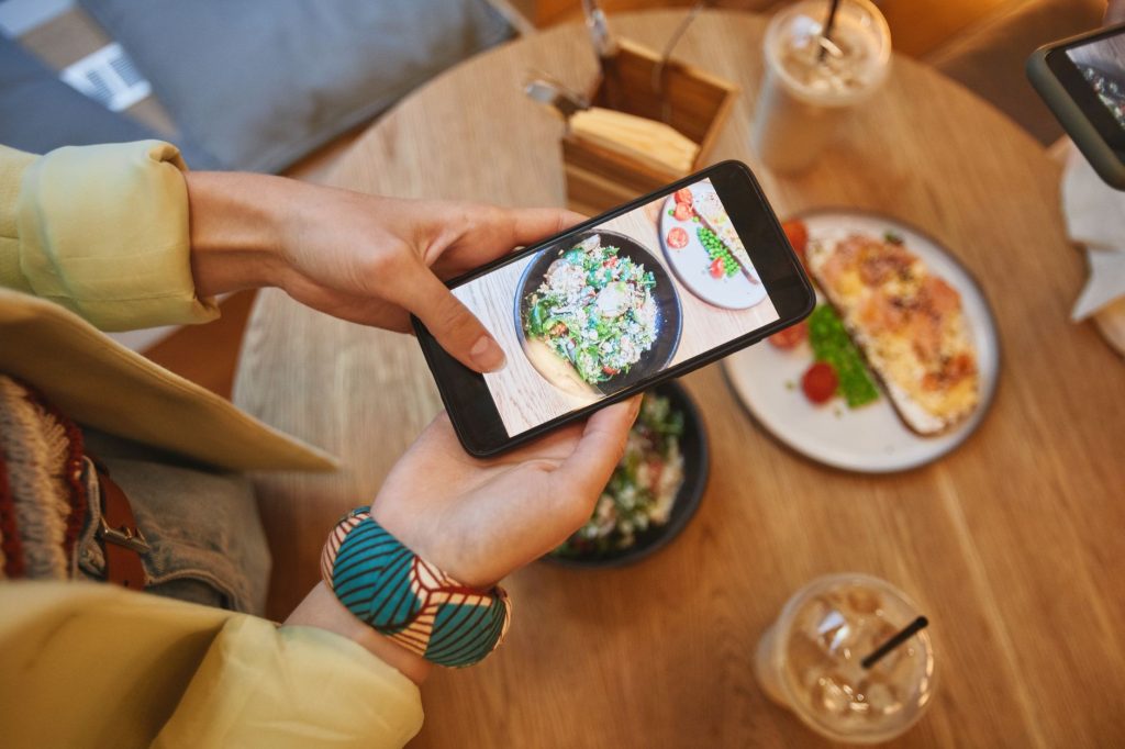 Person taking a photo of delicious meals on a smartphone in a cozy cafe setting.