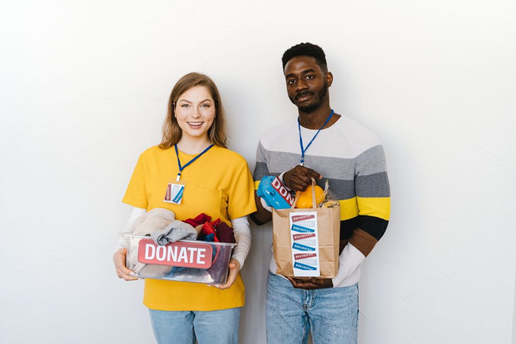Two diverse volunteers smiling while holding donation boxes indoors with a white background.